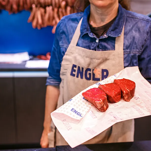 Mitarbeiterin präsentiert drei rohe Fleischstücke auf Papier.