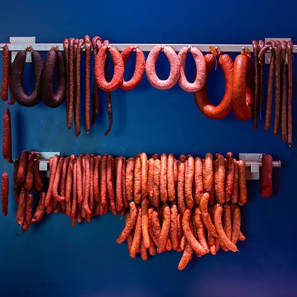 Vielfalt an Wurstsorten aufgehängt vor blauer Wand.