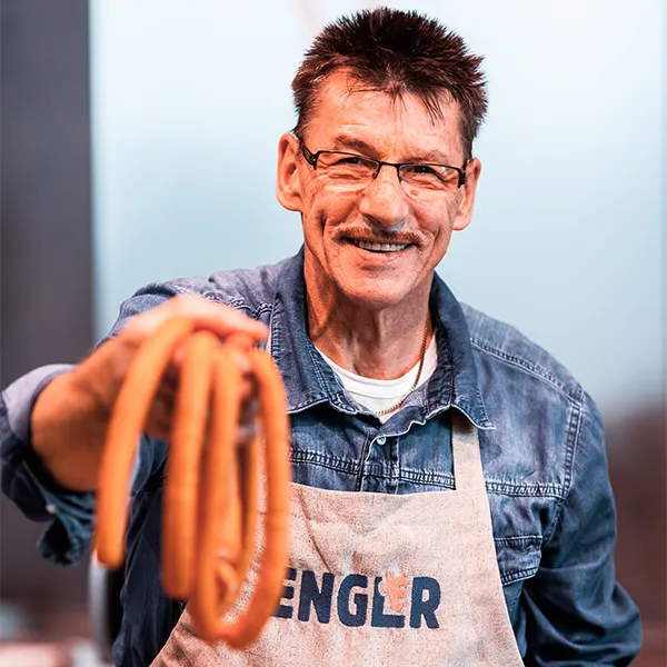 Mitarbeiter hält mehrere Wienerle in der Handy und lächelt.