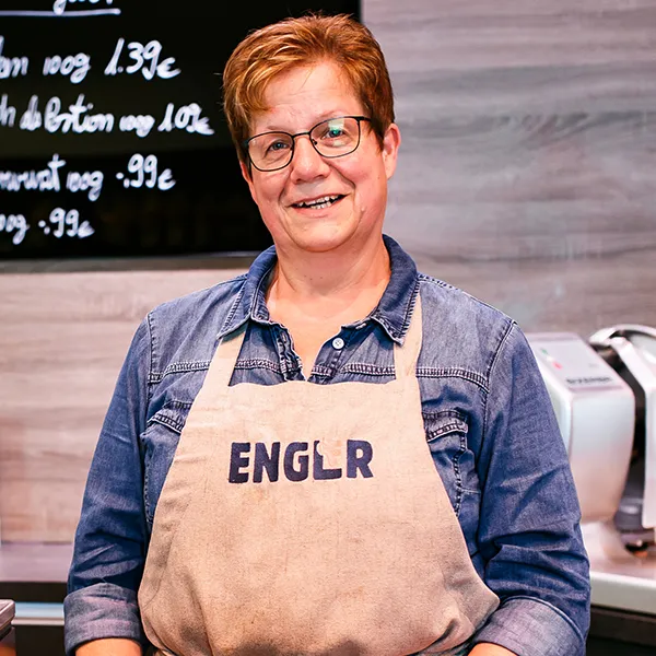 Mitarbeiterin mit Schürze lächelt an der Theke.