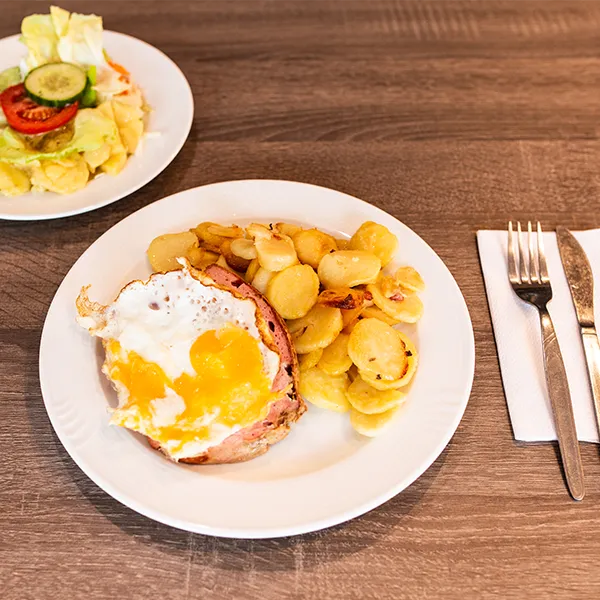 Gebratener Leberkäse mit Spiegelei und Bratkartoffeln auf weißem Teller.